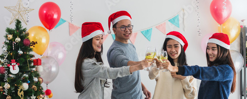 Young Asian man and beautiful Asian woman drink champagne celebration with best friend.Smiling face in room with Christmas tree decoration for holiday festival.Christmas Party and celebration concept.