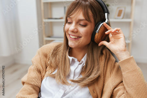 Cute happy young blonde student lady freelancer in warm sweater wear headphones enjoy fav songs sitting in armchair at modern home interior. Music time Relaxing Cool playlist Concept. Copy space photo