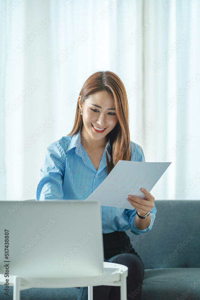 Portrait of a smiling Asian woman sitting on a sofa. Using laptop in the living room at home, working at home via online video conference. Portrait of a smiling Asian woman sitting on a sofa. Using laptop in the living room at home, working at home via online video conference.