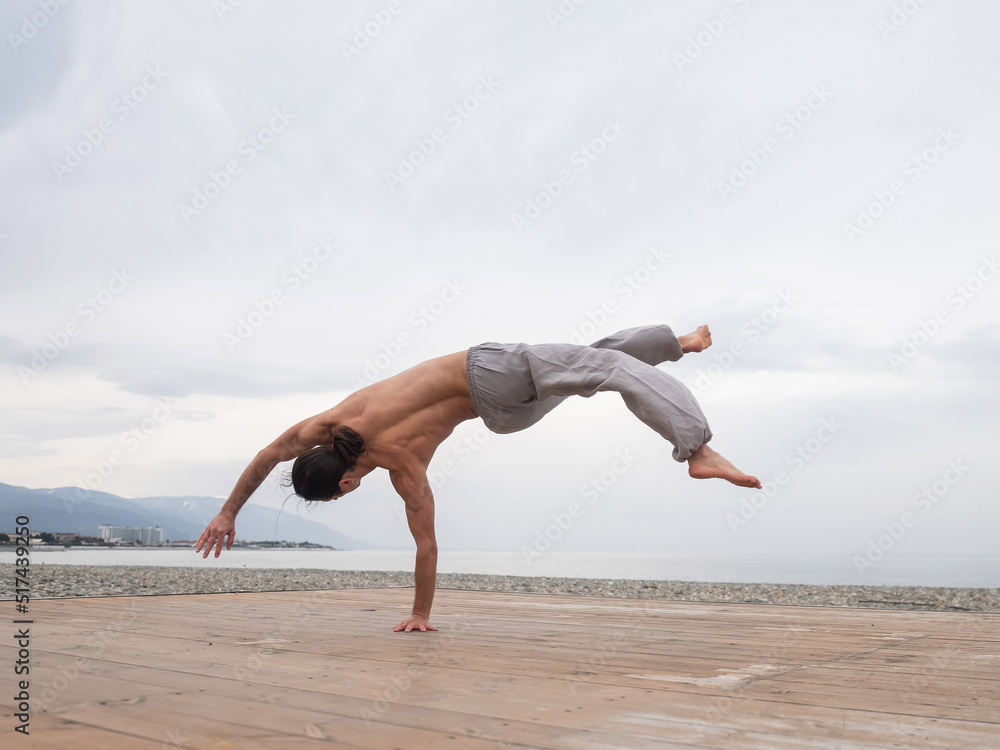 Fototapeta premium Shirtless caucasian man doing backflip on pebble beach. 