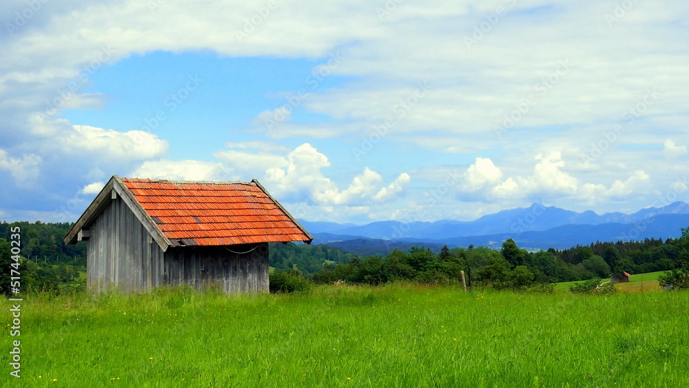 zartes Morgenlicht strahlt alte Holzhütte auf Wiese im Ammergau unter blauem Himmel und Wolken an zartes Morgenlicht strahlt alte Holzhütte auf Wiese im Ammergau unter blauem Himmel und Wolken an