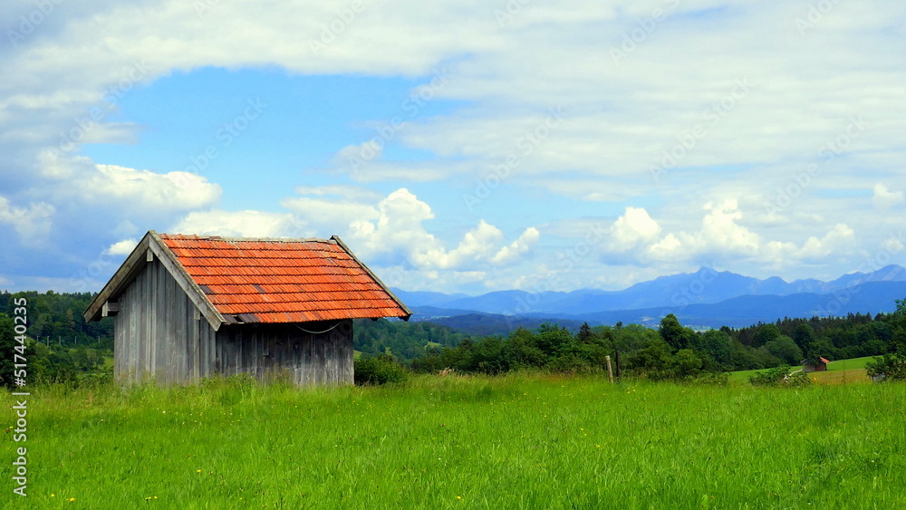 zartes Morgenlicht strahlt alte Holzhütte auf Wiese im Ammergau unter blauem Himmel und Wolken an