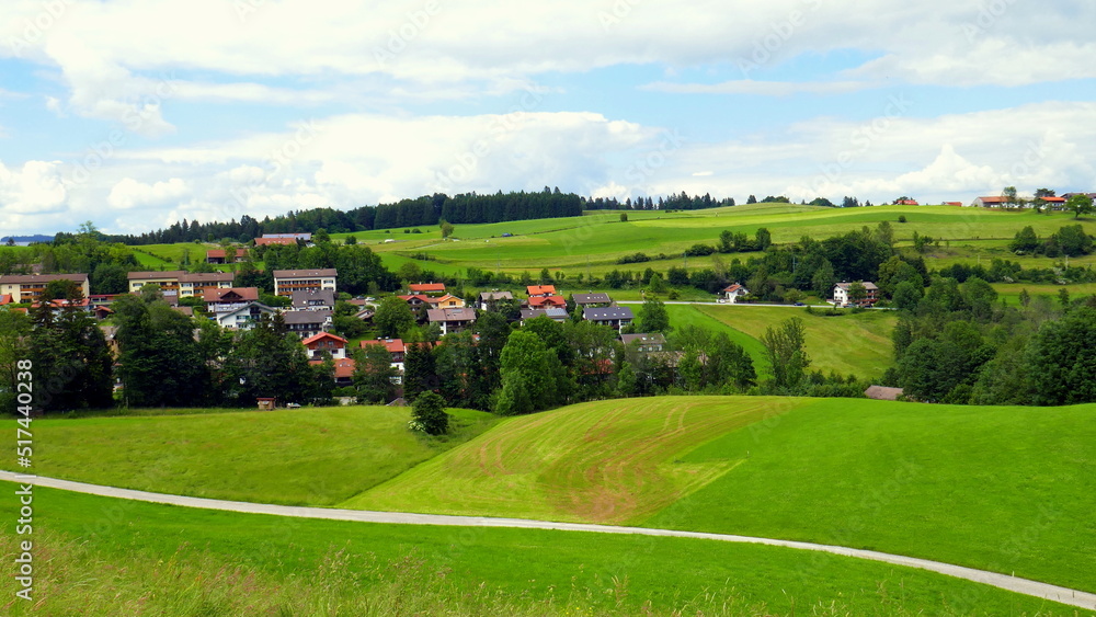 Panorama von Bad Kohlgrub im Ammergau mit Häusern, Wald, Weg und grünen Wiesen am Morgen