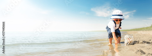Kid play on the beach on a hot sunny day. Little girl walks barefoot along the sandy seashore and collects shells in a jar.