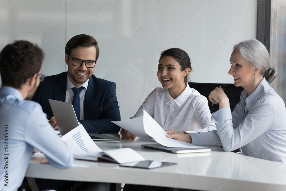 Happy different aged diverse business group negotiating on marketing reports, talking, discussing startup project strategy, laughing, brainstorming. HR team interviewing job candidate Happy different aged diverse business group negotiating on marketing reports, talking, discussing startup project strategy, laughing, brainstorming. HR team interviewing job candidate