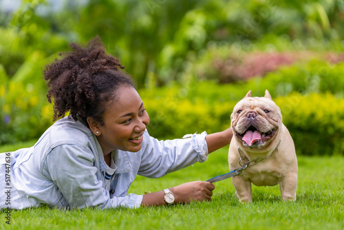 African American woman is playing with her french bulldog puppy while lying down in the grass lawn after having morning exercise in the park