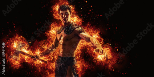 Portrait of burning barbarian with naked torso who posing holding axe in dark studio background