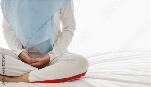 Close up young asian woman hand sitting on bed and enjoying meditation. Beautiful girl in muslim sleepwear with blue hijab practices yoga in bedroom with peace and calm. Healthy and lifestyle concept