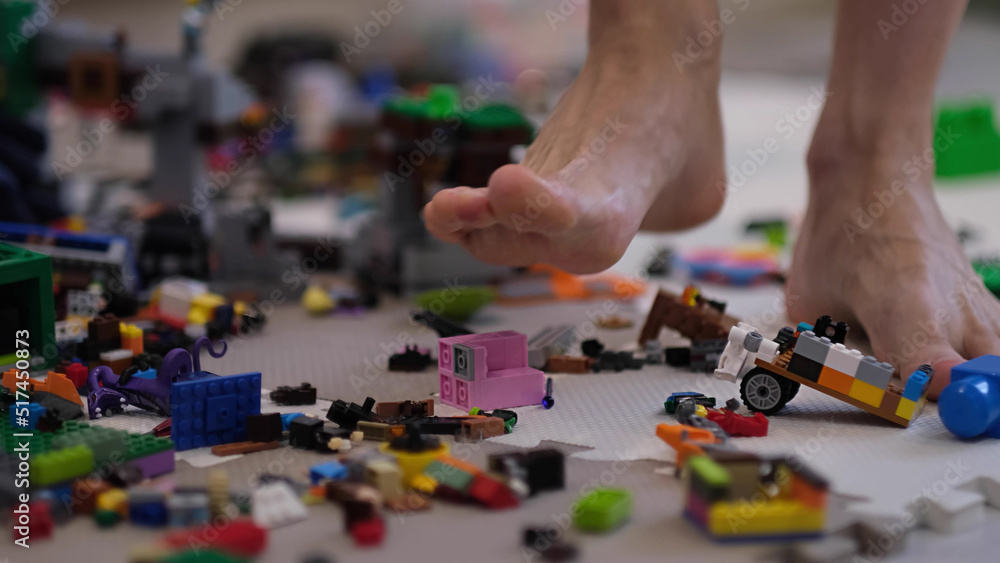 barefoot man walks among the scattered toys. Foot stepping on children's toys. Scattered toys on the floor. concept of an abundance of toys in the modern world. barefoot man walks among the scattered toys. Foot stepping on children's toys. Scattered toys on the floor. concept of an abundance of toys in the modern world.