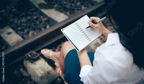 Holiday event in summer, young asian woman sitting near the train tracks and writing her diary before leaving for a trip by train