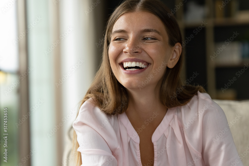 Laughing pretty young woman staring aside looks overjoyed, vivacious sits on sofa, close up shot. Happy renter, homeowner portrait, relaxation at modern home, natural beauty, candid emotions concept Laughing pretty young woman staring aside looks overjoyed, vivacious sits on sofa, close up shot. Happy renter, homeowner portrait, relaxation at modern home, natural beauty, candid emotions concept
