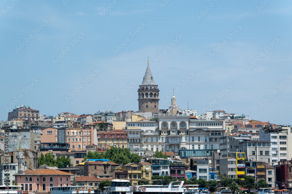 Galata Tower behind buildings front side view from Golden Horn, travel concept in Istanbul city, beautiful landscape, known as Galata Kulesi, old historical structure in Istanbul, buildings and sky
