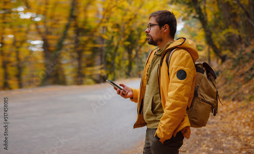 Young handsome man in autumn forest with smartphone. young hipster guy with backpack , traveller standing in woods, Hiking, Forest, Journey, active healthy lifestyle, adventure, vacation concept.