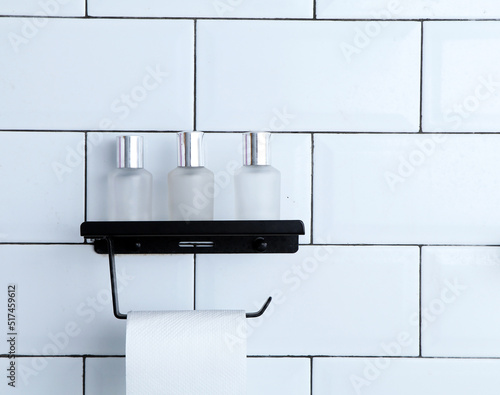 White-tiled bathroom with mock-up space for montage your brands, bathing accessories, and skincare tubes in a white modern bathroom. Toilet roll paper on the holder