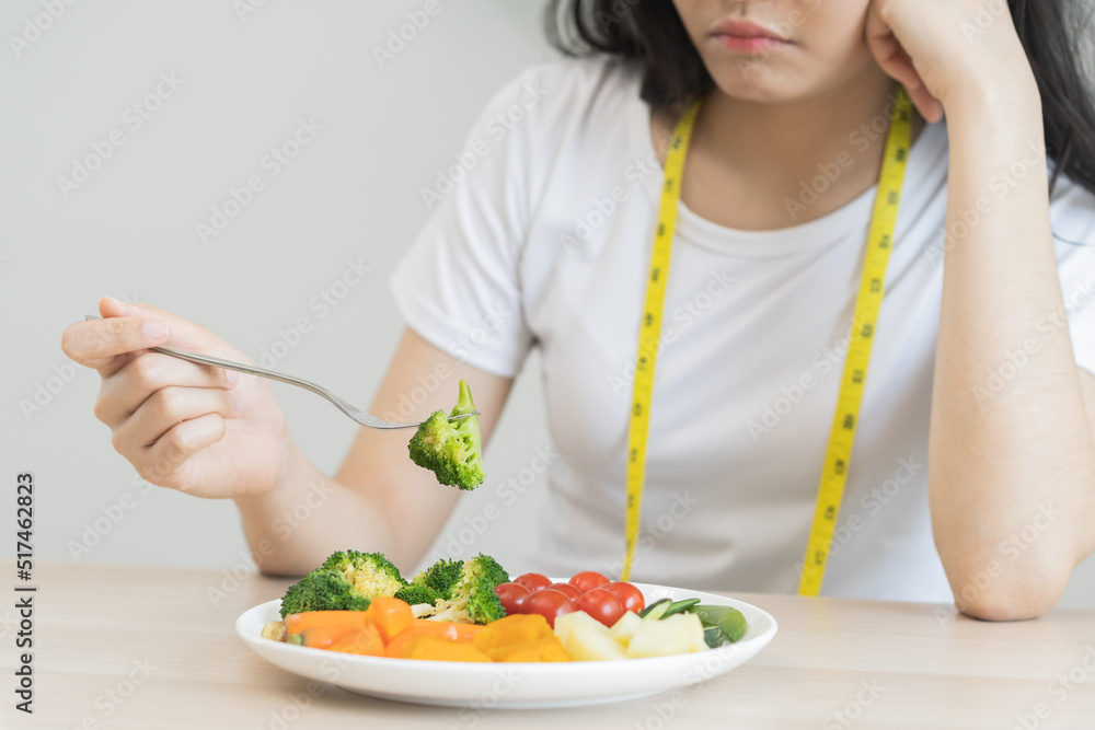 Diet in bored. Closeup broccoli unhappy beautiful asian young woman, girl on dieting, hand holding fork in salad plate, dislike or tired with eat fresh vegetables. Nutrition of healthy food good taste Diet in bored. Closeup broccoli unhappy beautiful asian young woman, girl on dieting, hand holding fork in salad plate, dislike or tired with eat fresh vegetables. Nutrition of healthy food good taste
