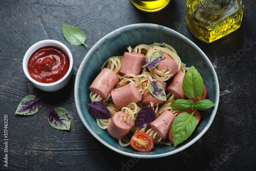 Green bowl with threaded hot dogs or sausage spaghetti, elevated view on a dark-brown stone background, studio shot
