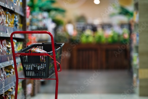 Water melon displayed and red shopping cart and goods in black basket near the shelf in supermarket