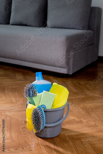 Bucket with cleaning items in the house, standing on the floor, on the background of the sofa. Housework. Cleaning