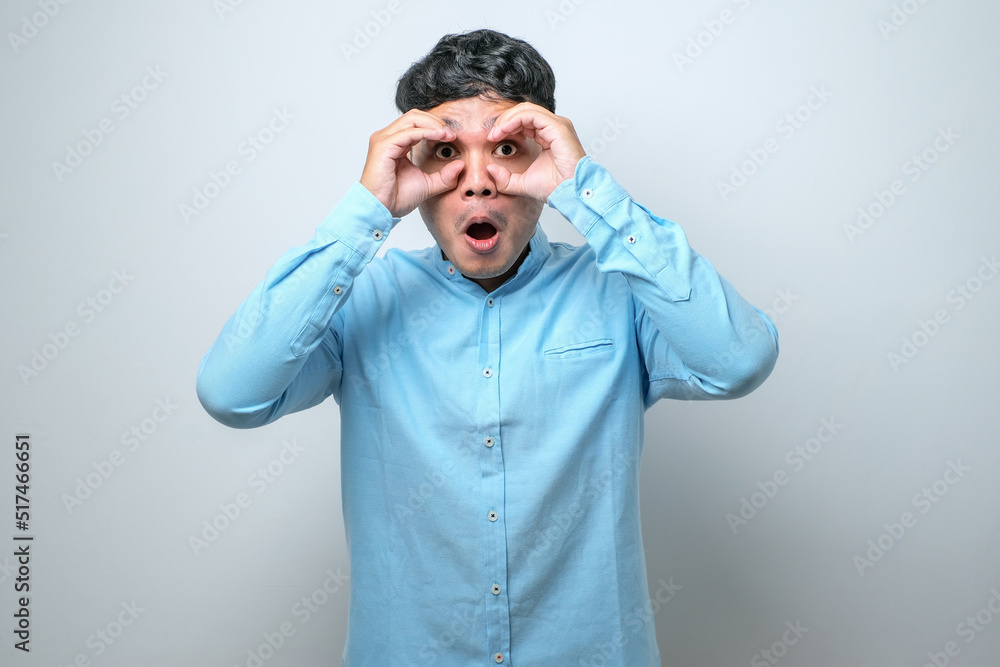 Young handsome man wearing casual shirt doing ok gesture like binoculars sticking tongue out, eyes looking through fingers.