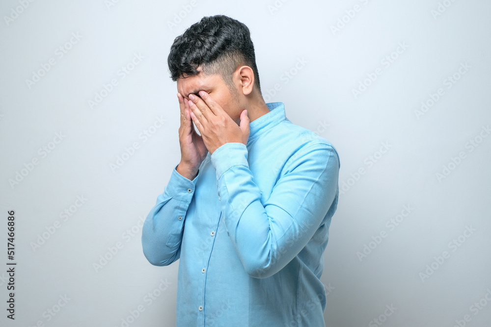 Asian young man with mustache wearing casual shirt with sad expression covering face with hands while crying. Asian young man with mustache wearing casual shirt with sad expression covering face with hands while crying.