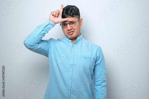 Young handsome man making fun of people with fingers on forehead doing loser gesture mocking and insulting.