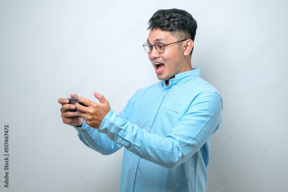 Shocked young good looking Asian man using smartphone to read good news online Shocked young good looking Asian man using smartphone to read good news online