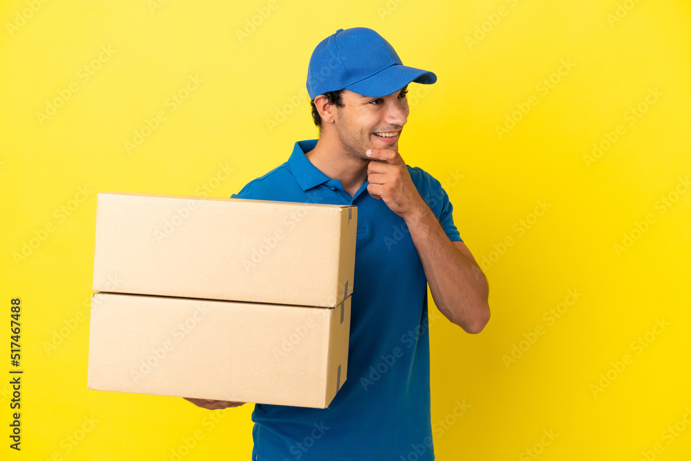 Delivery man over isolated yellow wall looking to the side and smiling Delivery man over isolated yellow wall looking to the side and smiling