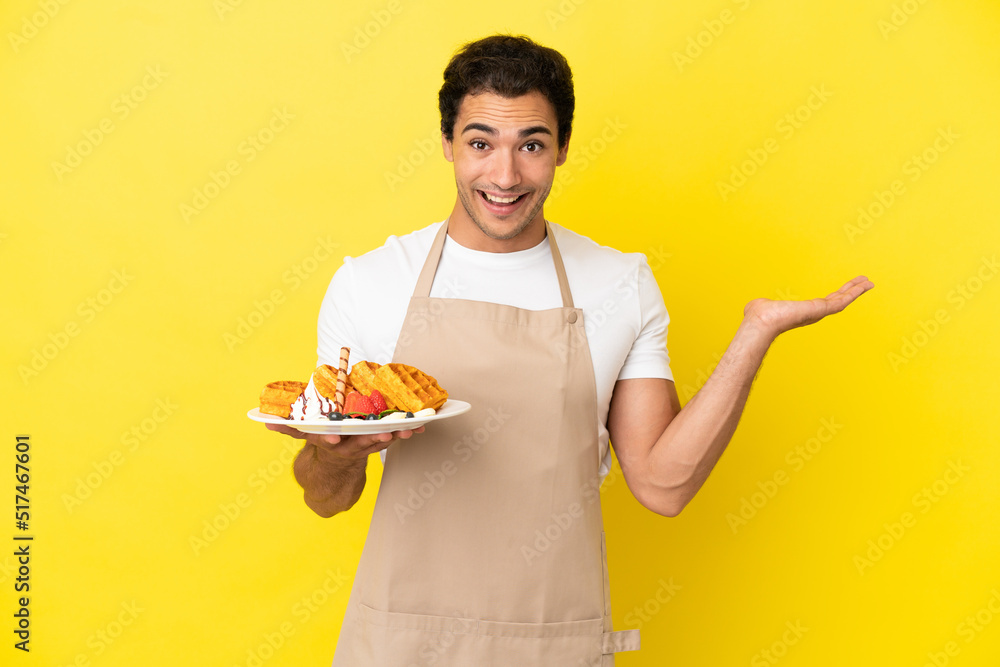 Restaurant waiter holding waffles over isolated yellow background with shocked facial expression Restaurant waiter holding waffles over isolated yellow background with shocked facial expression