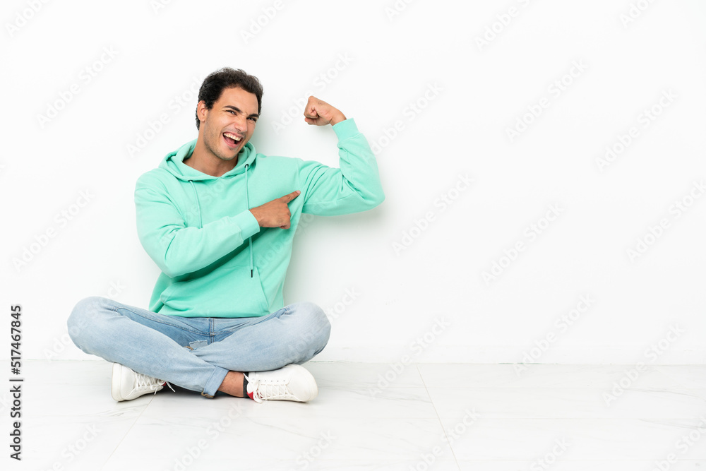Caucasian handsome man sitting on the floor doing strong gesture Caucasian handsome man sitting on the floor doing strong gesture