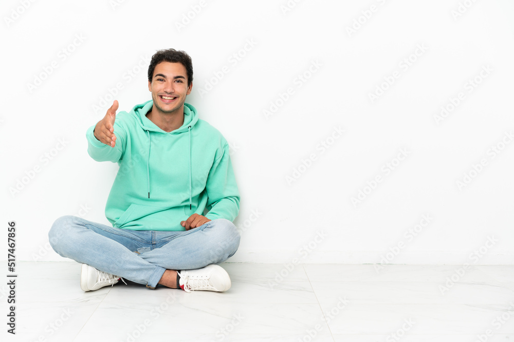 Caucasian handsome man sitting on the floor shaking hands for closing a good deal Caucasian handsome man sitting on the floor shaking hands for closing a good deal