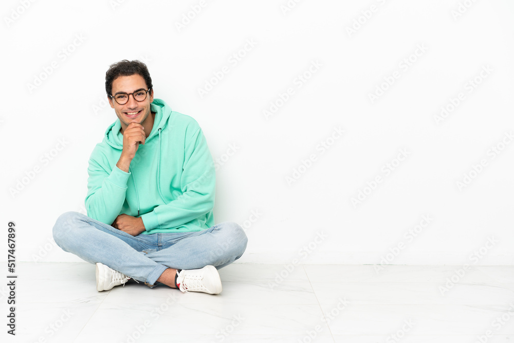 Caucasian handsome man sitting on the floor with glasses and smiling