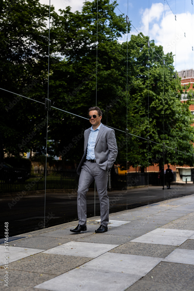 A handsome businessman in a grey suit and sunglasses in an urban city environment