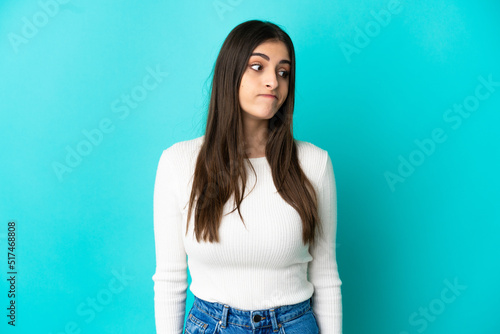 Young caucasian woman isolated on blue background making doubts gesture looking side
