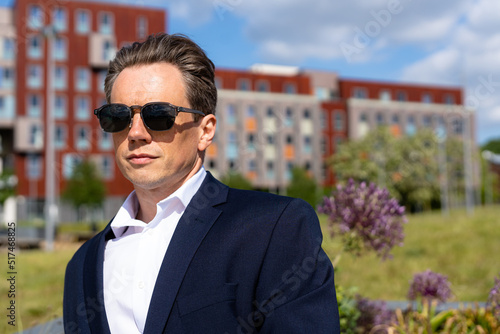 A handsome businessman in a casual dark blue suit in front of a residential area