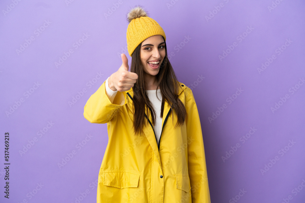 Young caucasian woman wearing a rainproof coat isolated on purple background with thumbs up because something good has happened
