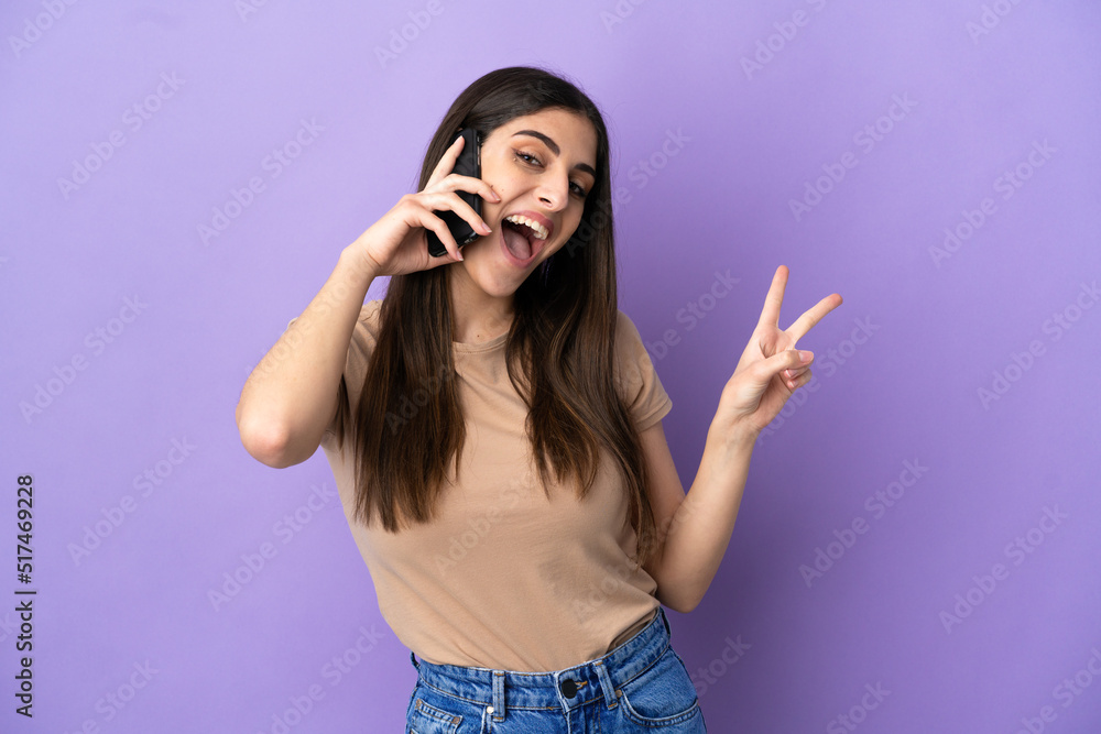 Young caucasian woman using mobile phone isolated on purple background smiling and showing victory sign Young caucasian woman using mobile phone isolated on purple background smiling and showing victory sign