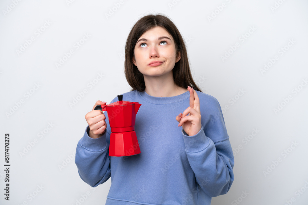 Young Russian woman holding coffee pot isolated on white background with fingers crossing and wishing the best Young Russian woman holding coffee pot isolated on white background with fingers crossing and wishing the best