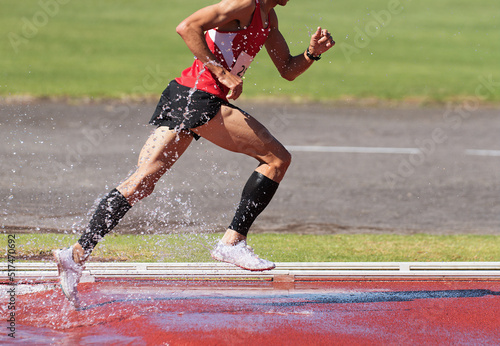 Runner running through the steeplechase water bake on a running track, steeplechase males athletes runner overcame water jump