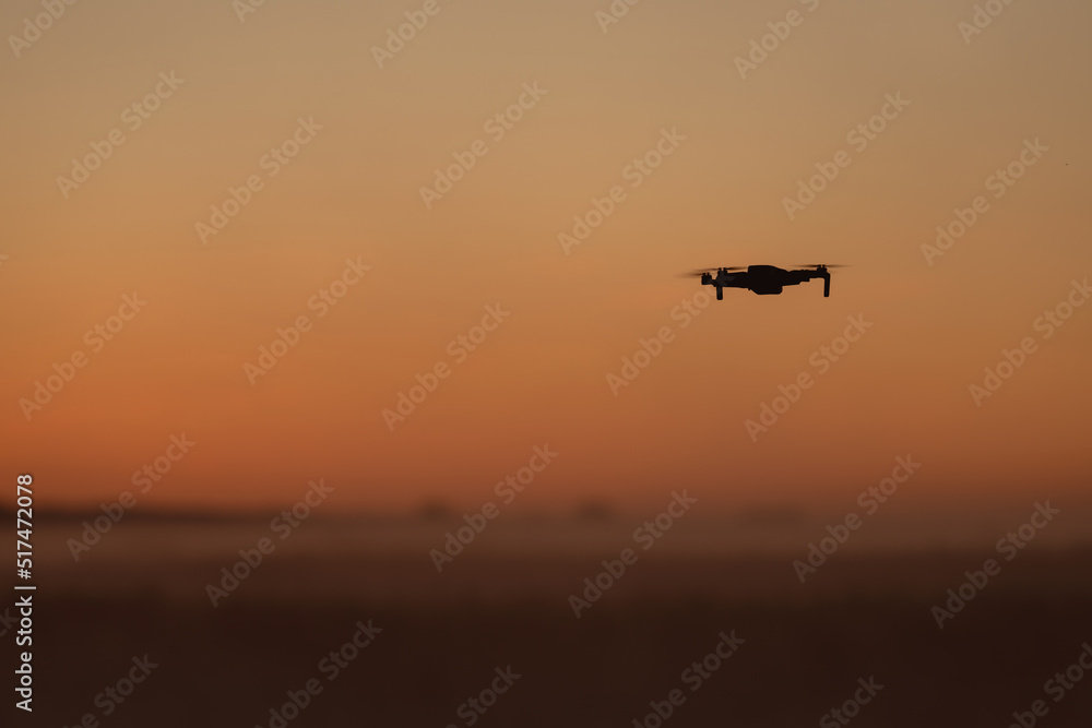 A quadcopter is flying in the fog in the orange sunset sky
