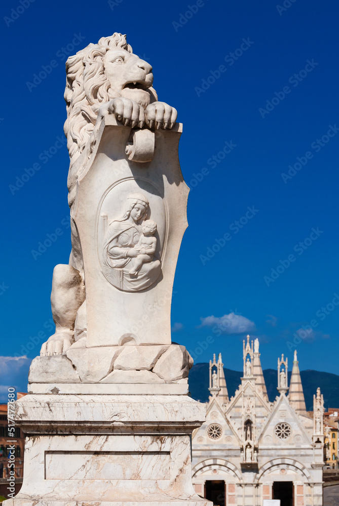 Marble lion statue, erected in 1875 in Pisa historical center, with beatiful St. Mary of the Thorn gothic church in the background