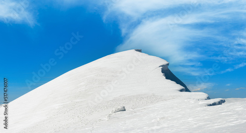 Winter mountains ridge with overhang snow caps and snowboard tracks on blue sky background (Ukraine, Carpathian Mt's, Svydovets Range, Blyznycja Mount, Drahobrat ski resort). 