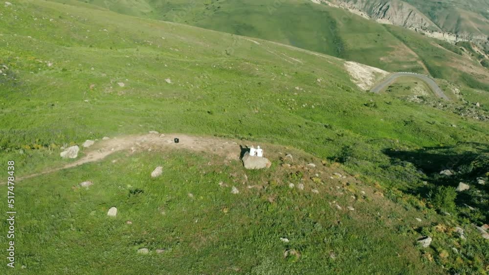 two people sit on the edge of a cliff and look at a beautiful mountain valley. Aerial shot fly around two people sit on the edge of a cliff and look at a beautiful mountain valley. Aerial shot fly around