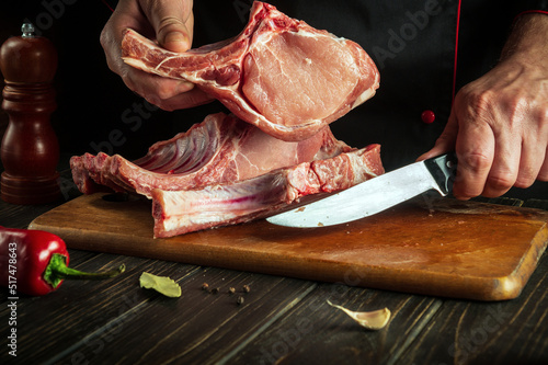 Butcher or experienced chef is holding a piece of raw meat with a bone in the kitchen. Slicing pork ribs by the hands of a butcher