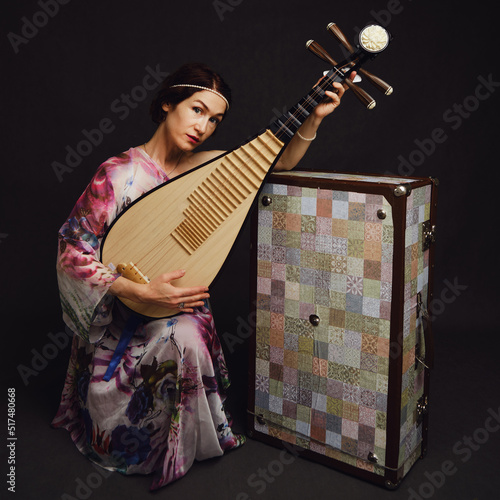 A happy female musician in Asian clothes on a studio black background. A smiling woman with a stringed musical instrument from Asia on a dark background photo