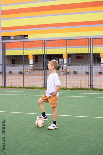 A teenage boy stands on a green field in the school yard with a soccer ball