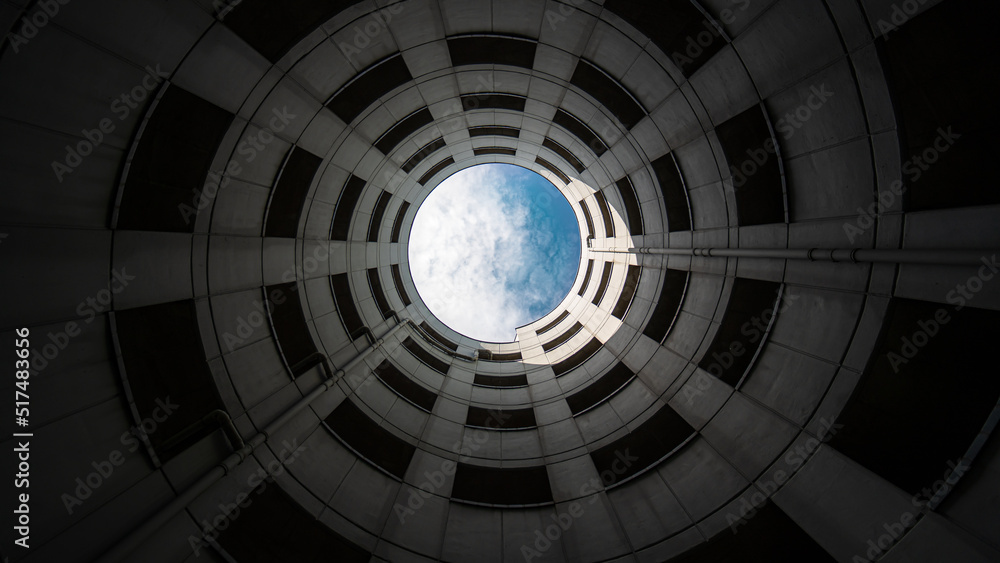 Spiral entrance tube of a parking garage made of concrete with view of blue sky and white clouds. Wide angle shot from bottom to top