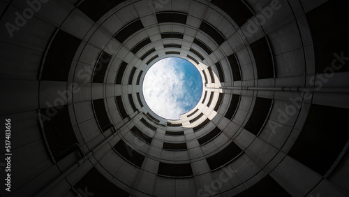 Spiral entrance tube of a parking garage made of concrete with view of blue sky and white clouds. Wide angle shot from bottom to top