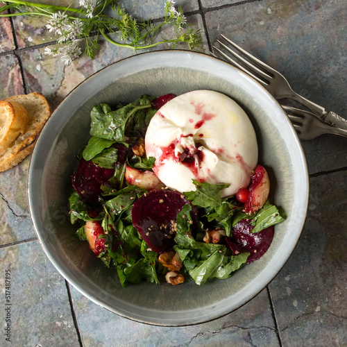 bowl with salad with baked beets, fruits, walnuts and buratta cheese on the table on the table