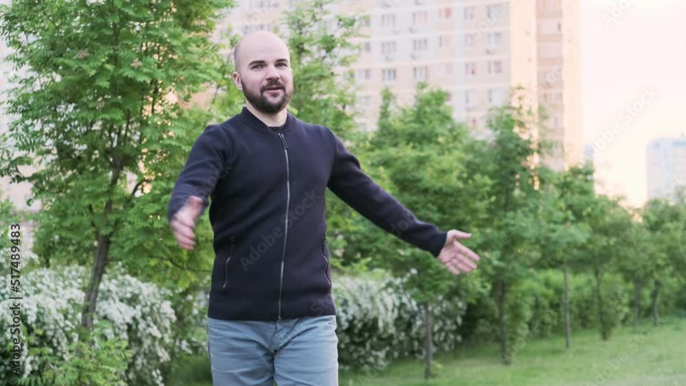 A man raises his hands and spins in the park against the background of trees and bushes
A man raises his hands and spins in the park against the background of trees and bushes