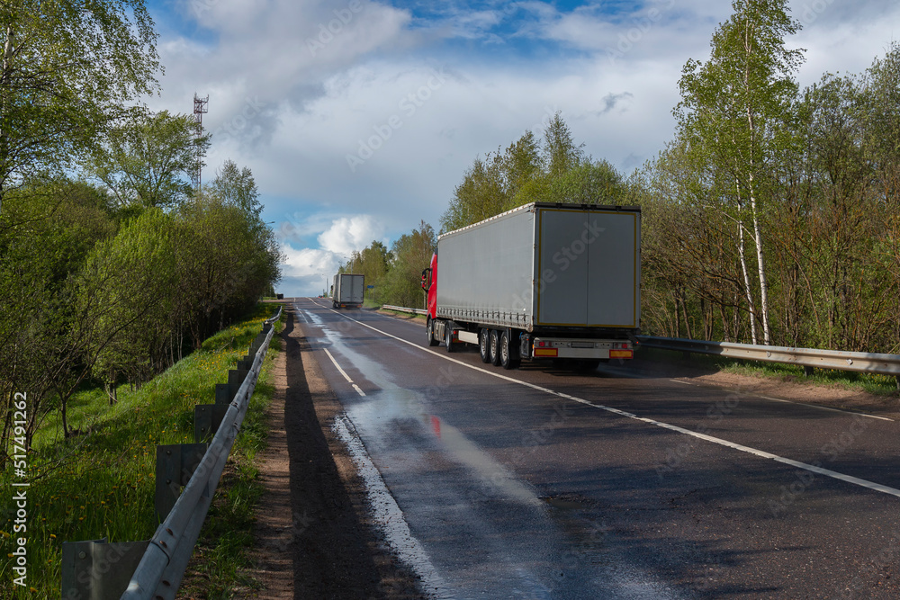 A shot from wayside of trucks on a road in a forest against the sky by summer day A shot from wayside of trucks on a road in a forest against the sky by summer day